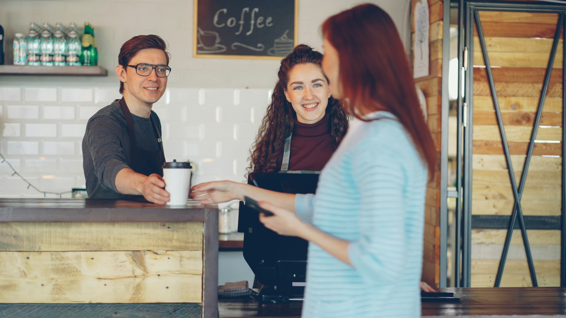 Café staff handing a takeaway coffee to a customer at the counter; illustrative small-business photography